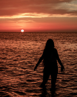 Silhouette of woman standing in ocean with red light from the sun.