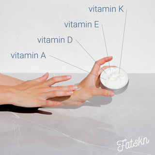 Picture of a field in the background with a baby in the foreground holding two tin cans of the product Fatskn, which is skin cream made from grassfed tallow.